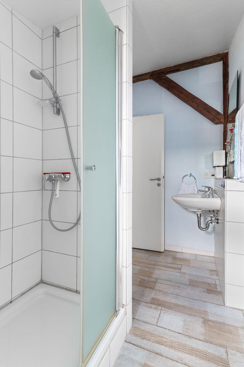 Bad mit Dusche, Waschbecken und Holzbalken an der Wand