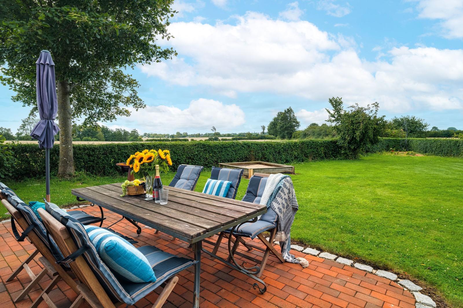 Terrasse mit Tisch, Stühlen und Sonnenblumen. Grünfläche und Hedges im Hintergrund.