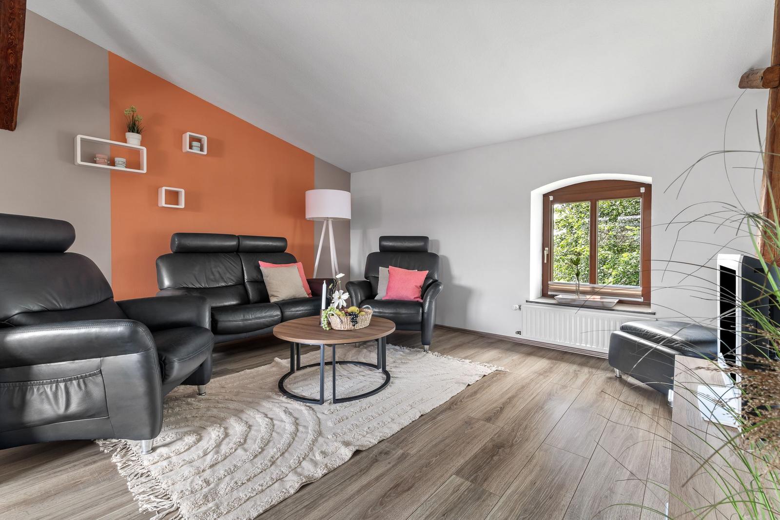 Wohnzimmer mit schwarzen Ledermöbeln, Holzboden und orangefarbener Wand.