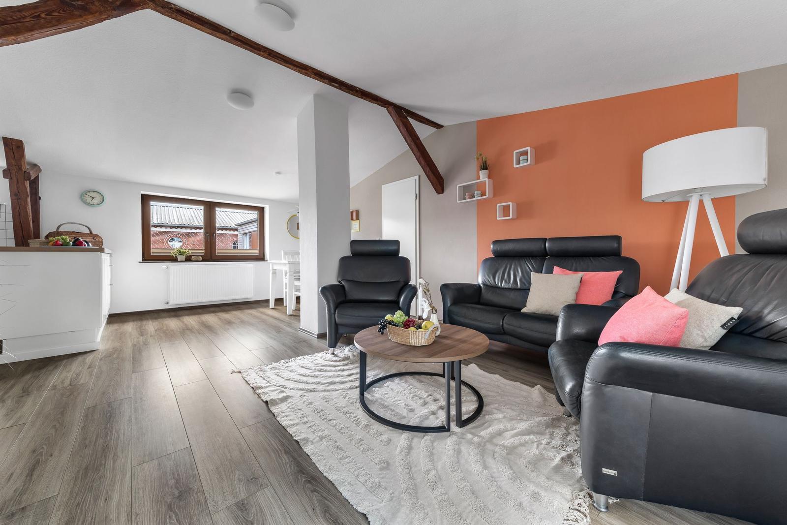 Wohnzimmer mit schwarzen Ledermöbeln, orangefarbener Wand und Holzboden.