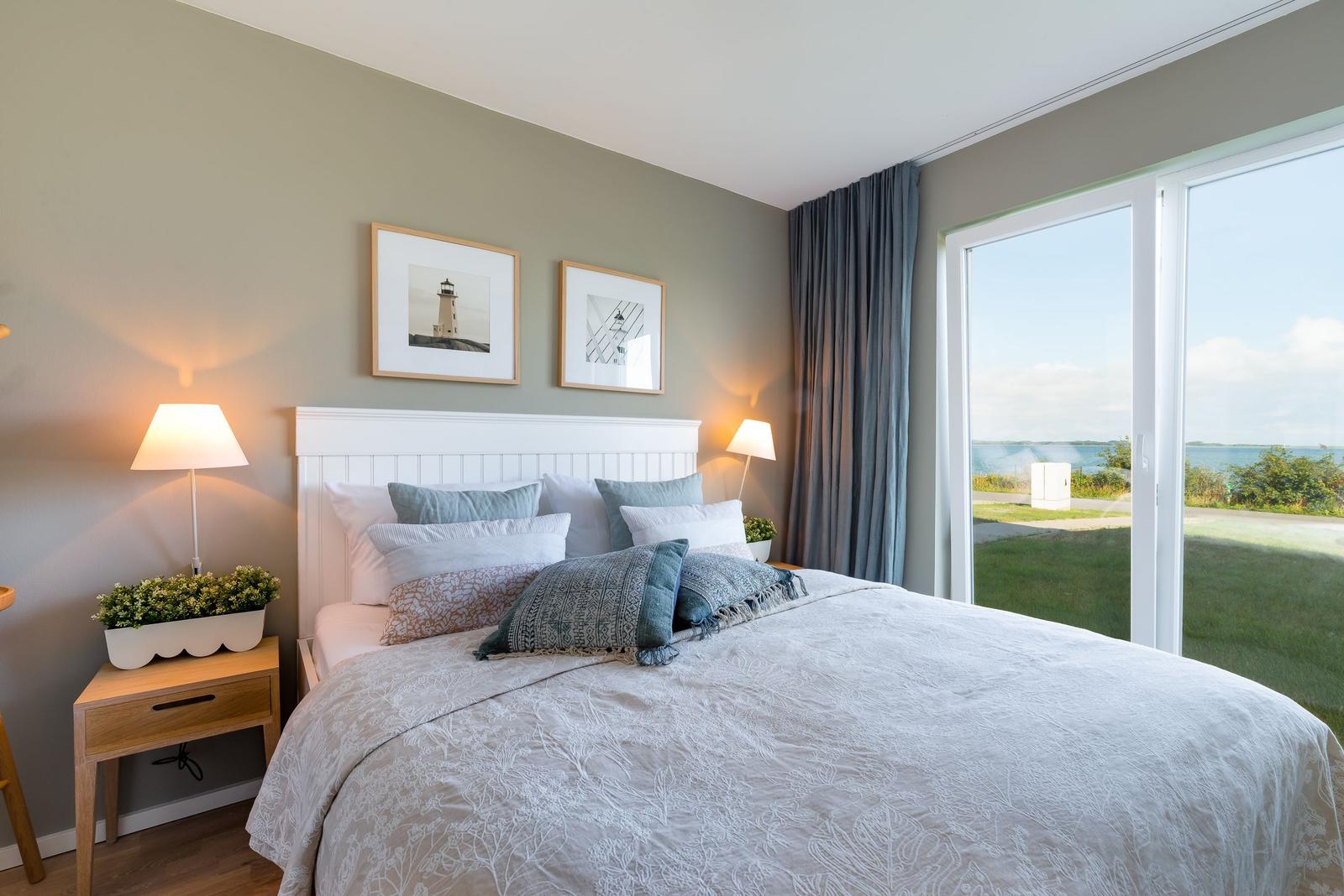Schlafzimmer mit Bett, Nachttisch und Blick auf den Strand.