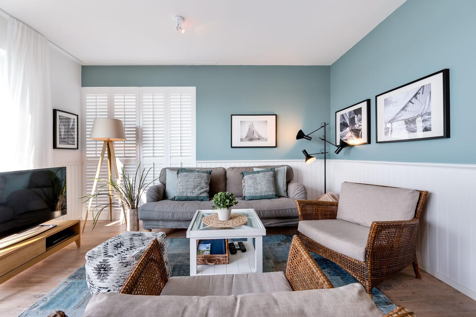 Wohnzimmer mit Sofa, Sessel und Couchtisch. Wandfarbe blau, Holzfußboden und Fenster mit Jalousien.