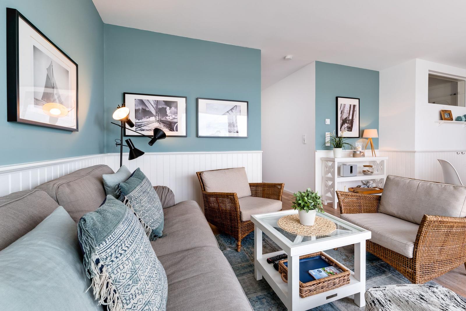 Wohnzimmer mit Sofa, Sessel und Couchtisch. Wandfarbe blau-weiß. Bilder an der Wand.