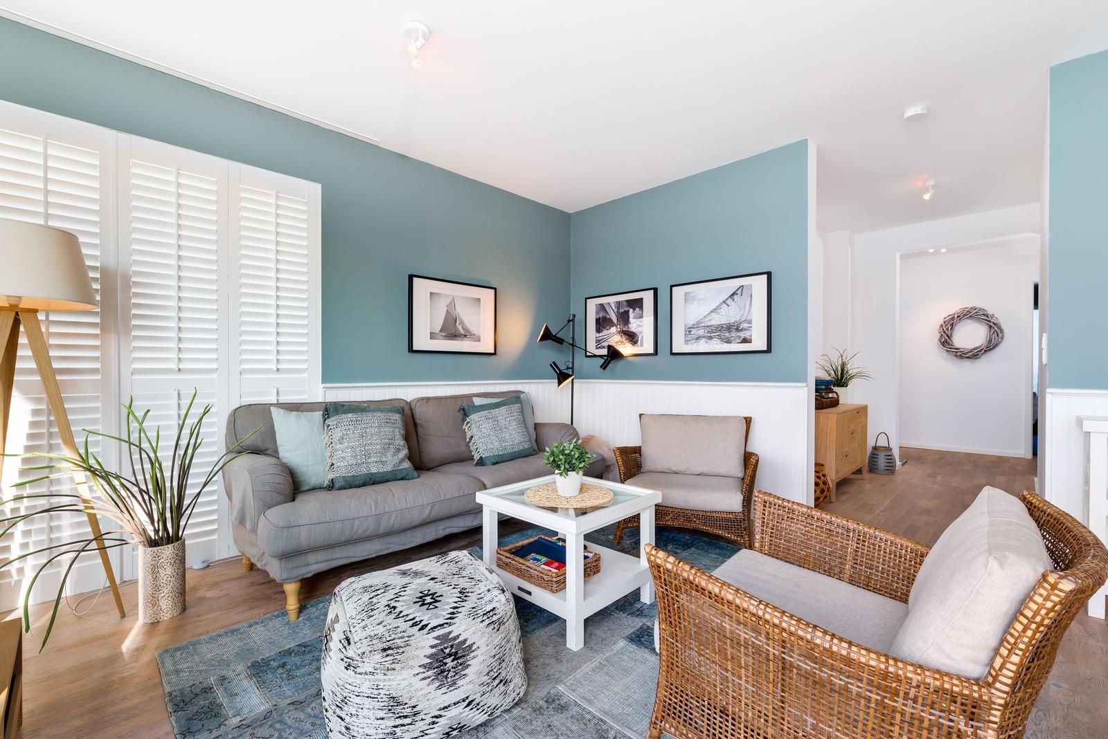 Wohnzimmer mit Sofa, Sessel und Tisch. Wandfarbe blau, Fenster mit Jalousien.
