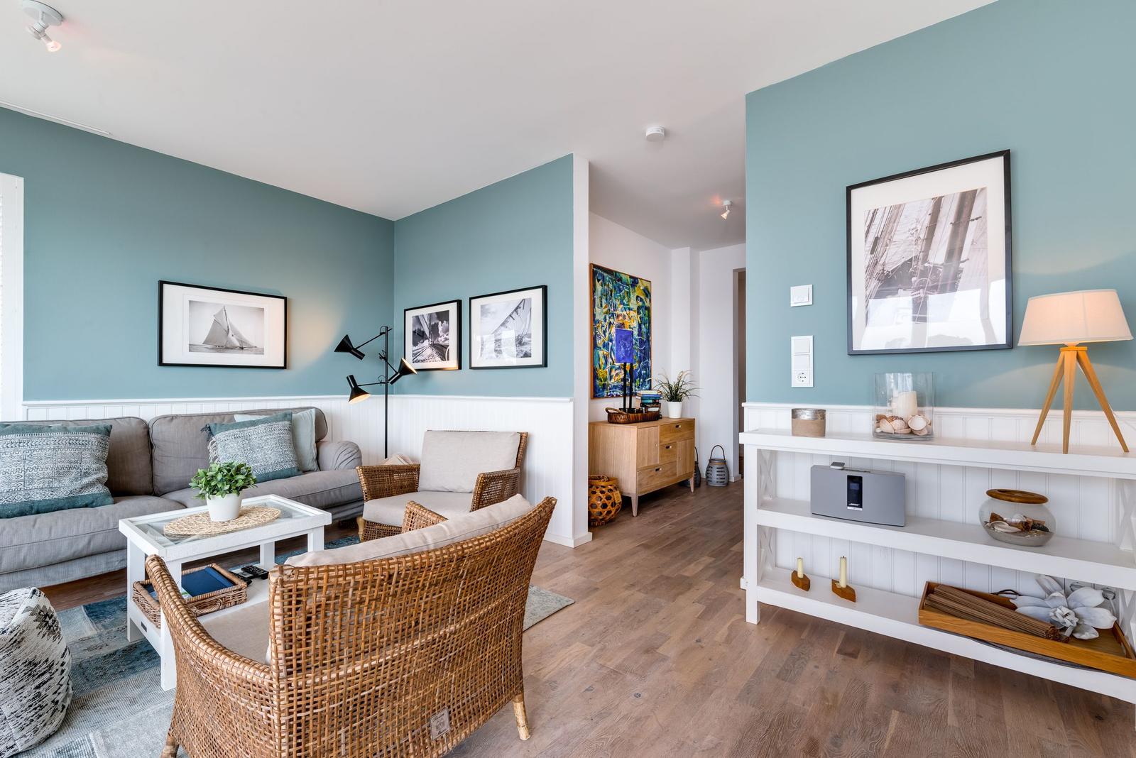 Wohnzimmer mit Sofa, Rattanmöbeln und Wandbildern an blauen Wänden.