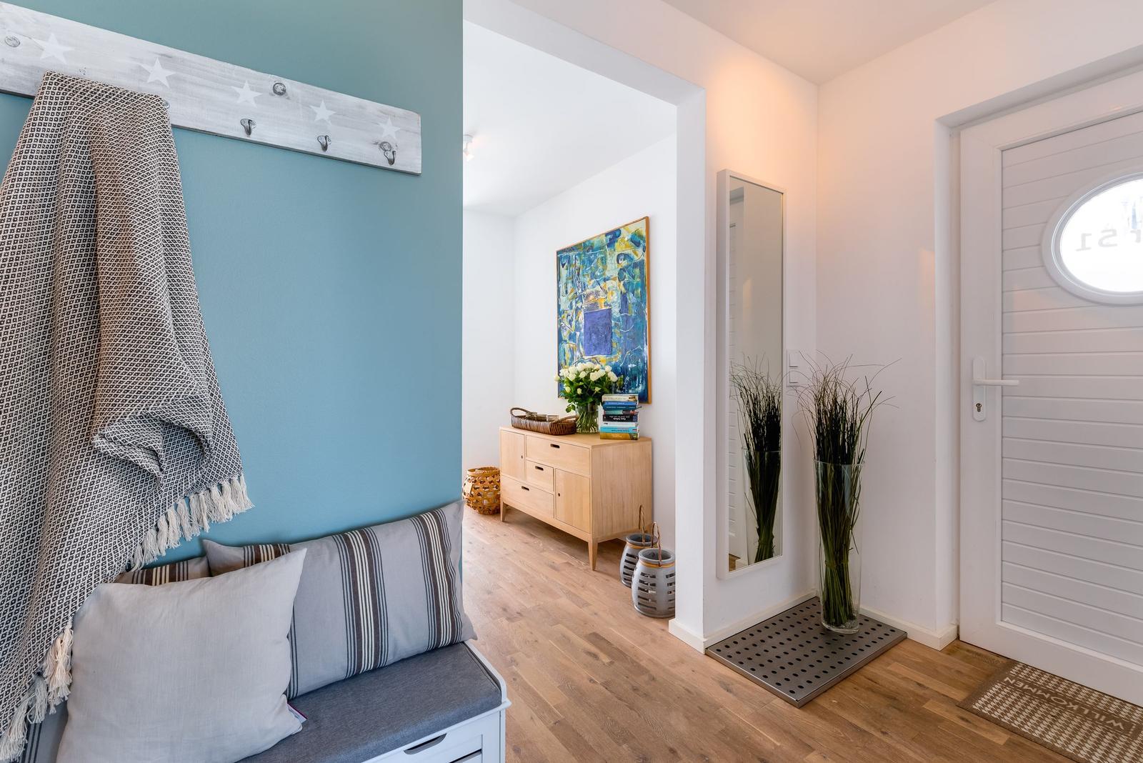 Eingangsbereich mit Sitzbank, Garderobe und Spiegel. Holzfußboden und weiße Wände.