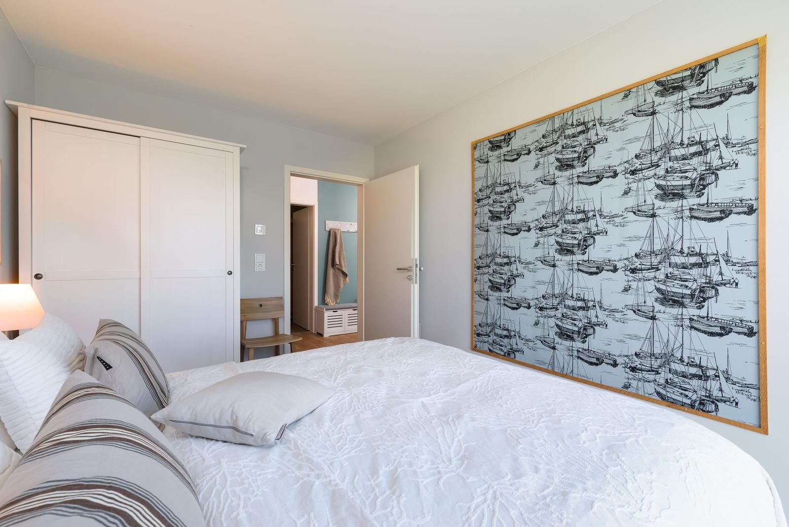 Schlafzimmer mit Bett, Kleiderschrank und Wandbild mit Schiffen.