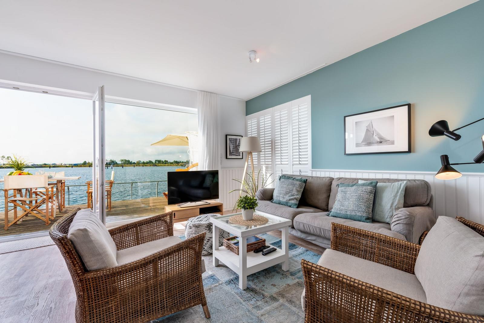Wohnzimmer mit Blick auf Wasser, Sofa, zwei Sessel und TV.