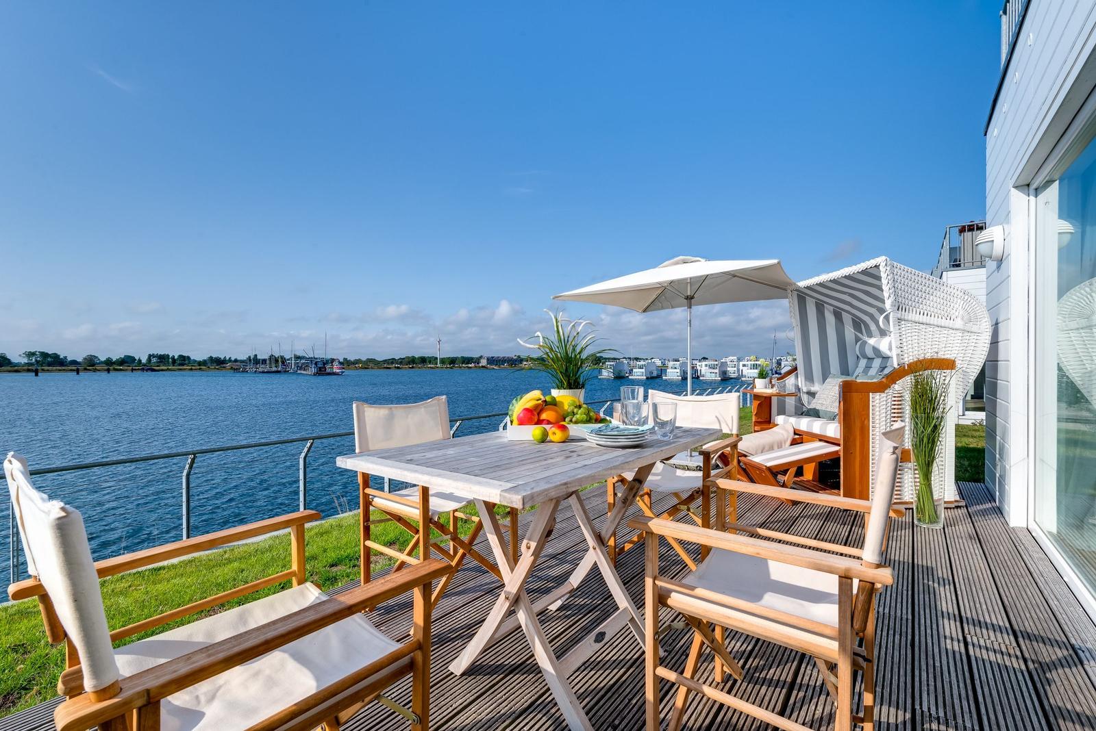 Terrasse mit Tisch, Stühlen und Sonnenschirm am Wasser