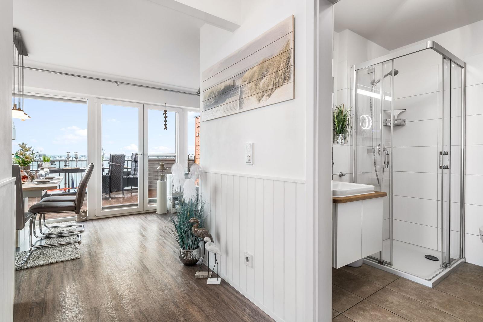 Wohnbereich mit Balkon und Badezimmer mit Dusche und Waschbecken.