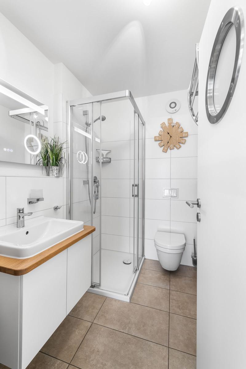Badezimmer mit Dusche, Waschbecken und Toilette. Holzoberfläche und runder Spiegel.
