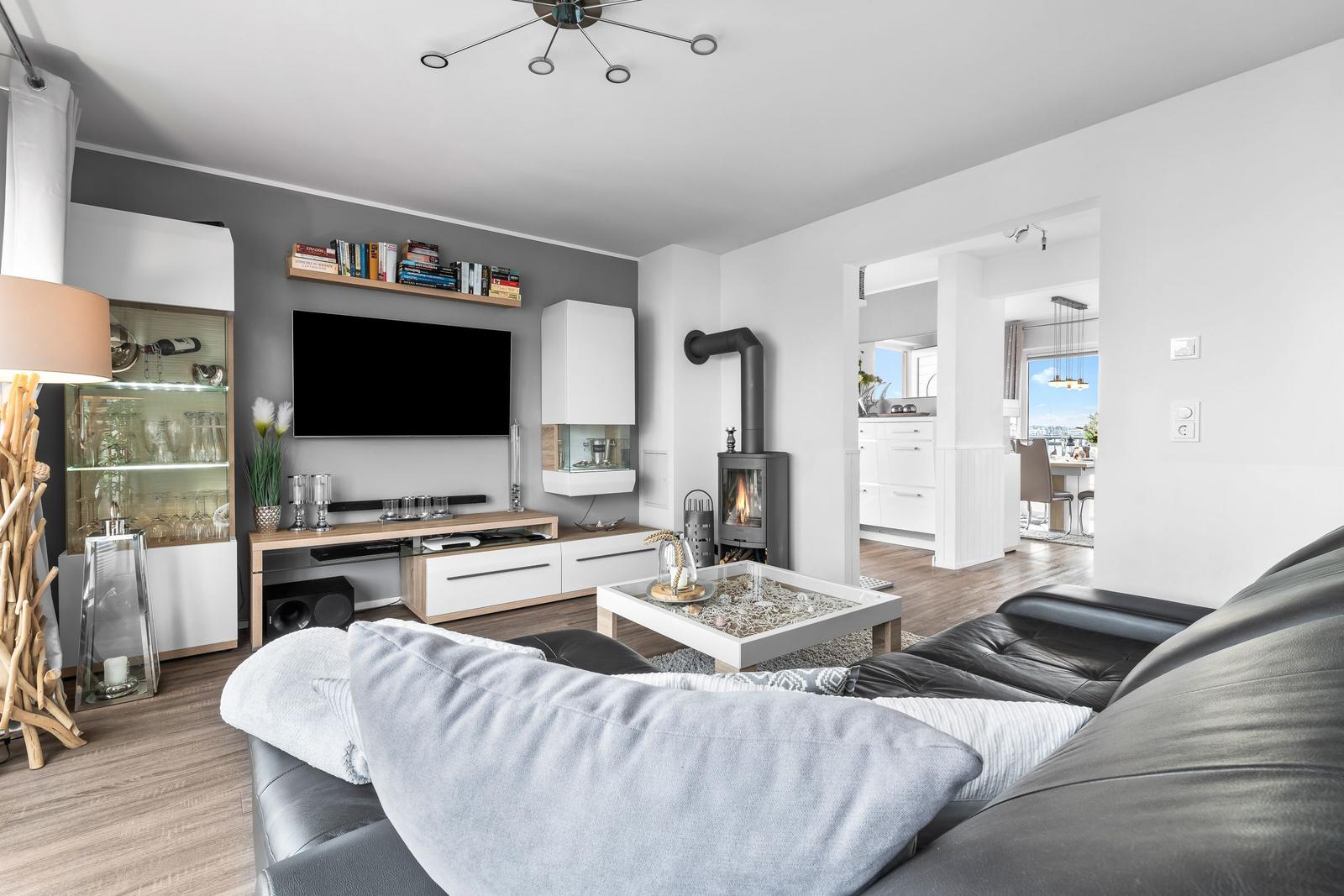 Wohnzimmer mit Sofa, Kamin und Fernseher. Küche und Essbereich im Hintergrund.