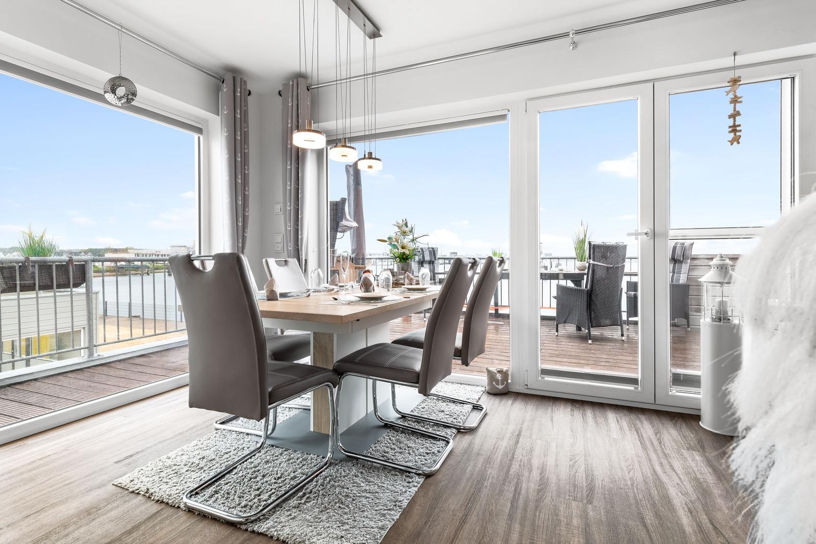 Essbereich mit Tisch und Stühlen, große Fenster zur Terrasse und Blick auf Wasser.