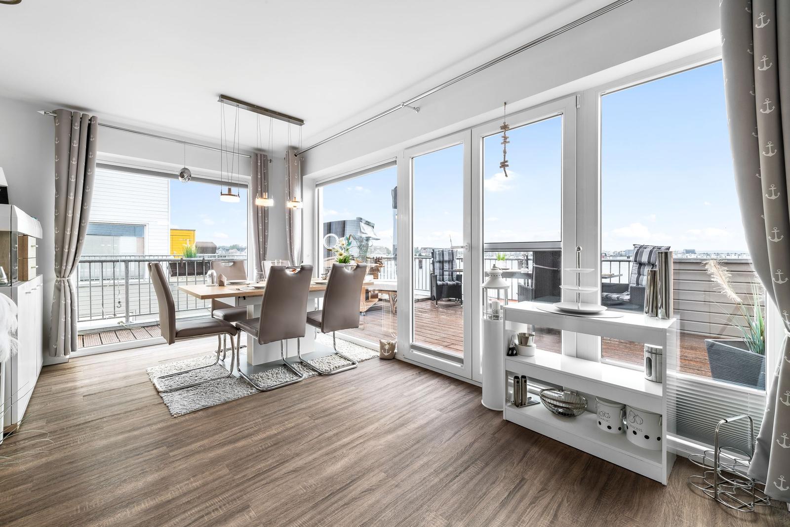 Essbereich mit Blick auf die Terrasse und Stadt. Holzboden, Fenster und Vorhänge.