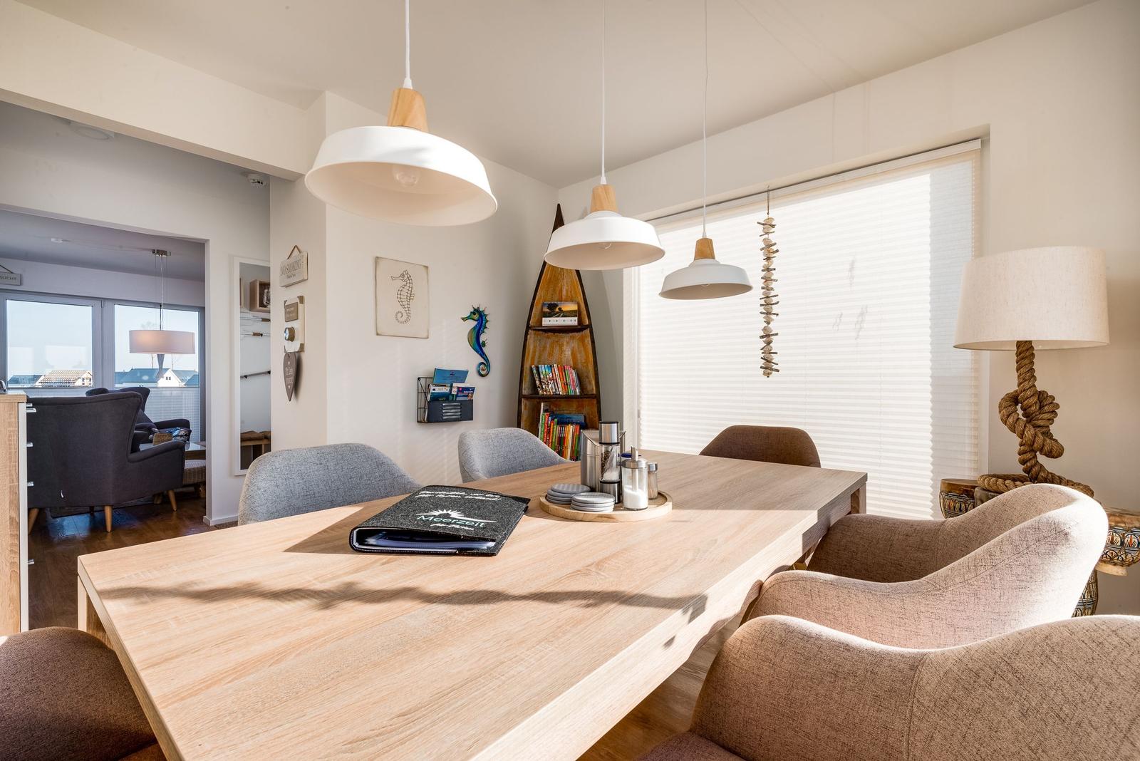 Essbereich mit Holztisch, Stühlen und hängenden Lampen. Fenster mit Jalousien und Seerosen-Dekoration.
