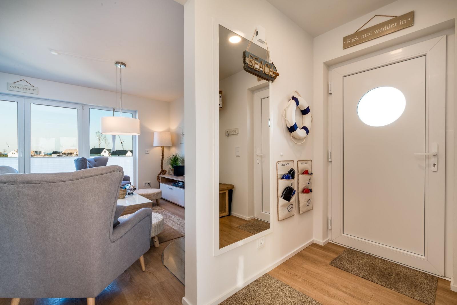 Eingangsbereich mit Tür und Spiegel. Wohnzimmer mit Sofa und Fenster.