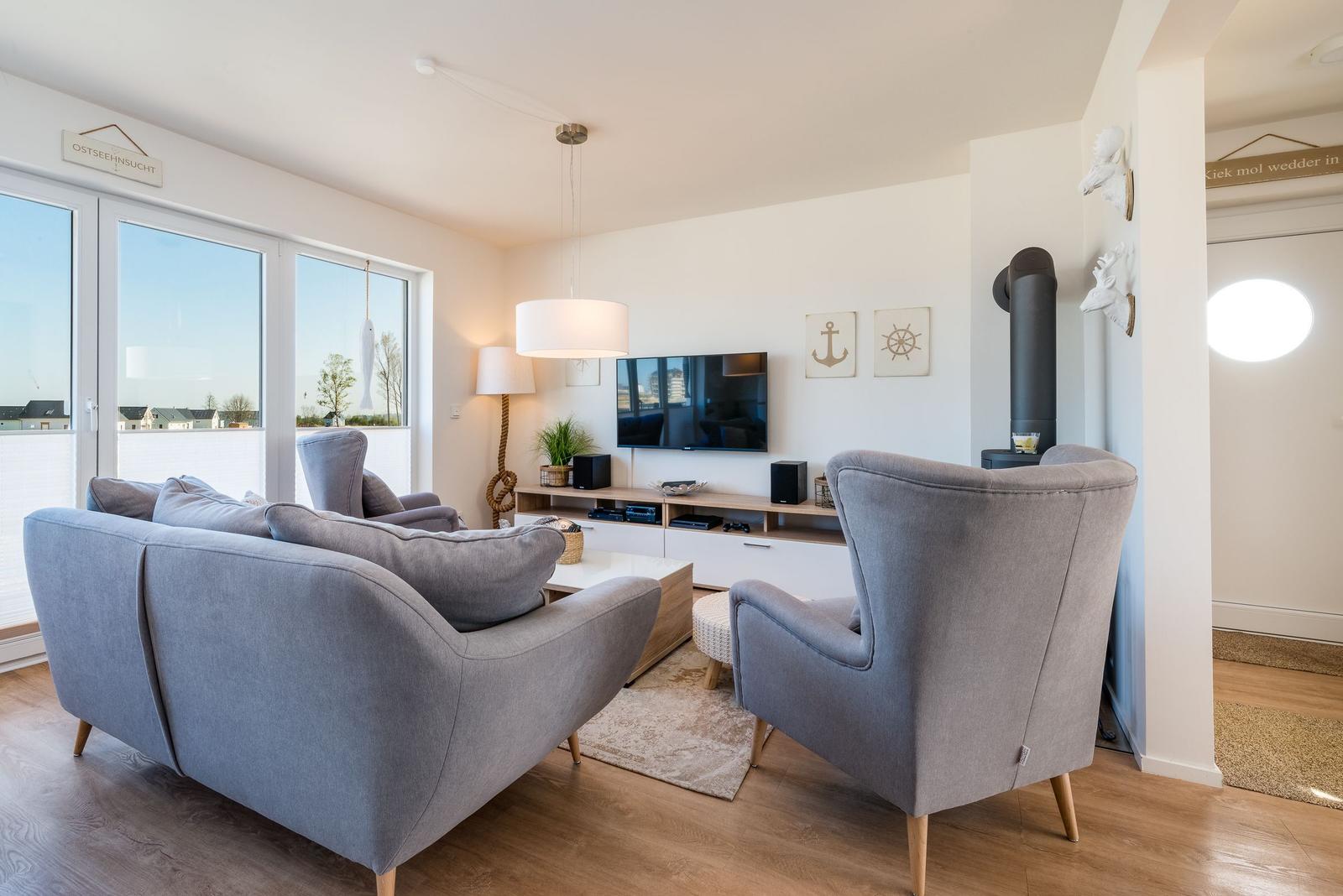 Wohnzimmer mit grauem Sofa, Fernseher und Holzboden. Große Fenster und Wandkamin.