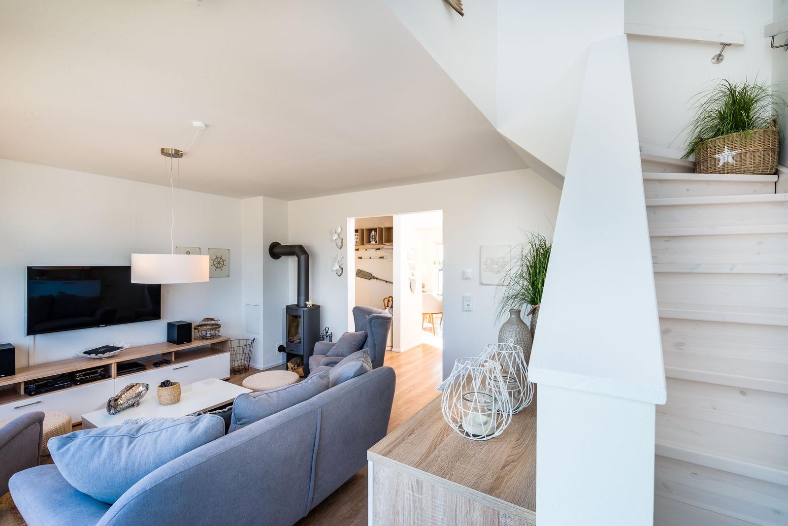 Wohnzimmer mit Sofa, Fernseher und Holztreppe. Im Hintergrund ist ein Kamin zu sehen.