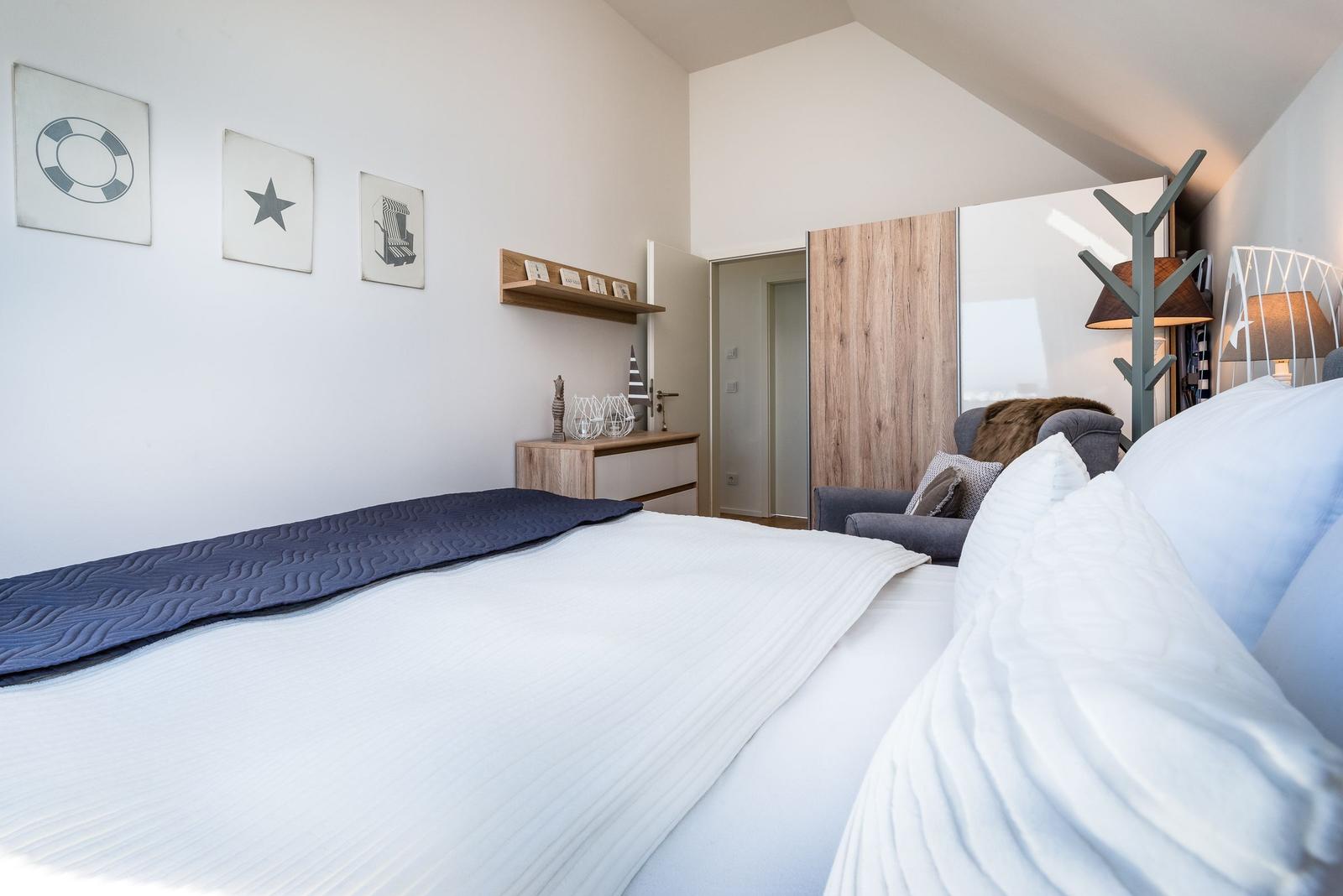 Schlafzimmer mit Bett, Wandbildern und Schrank. Holzregal und Beleuchtung sichtbar.