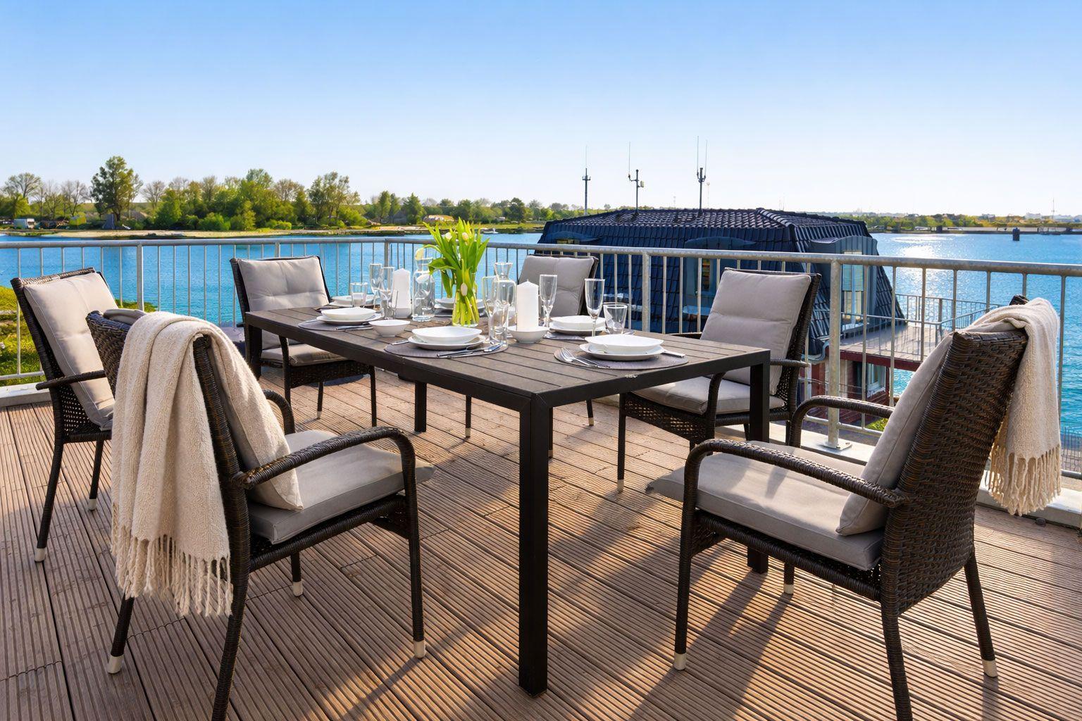 Terrasse mit Tisch und Stühlen, Blick auf Wasser und Ufer.