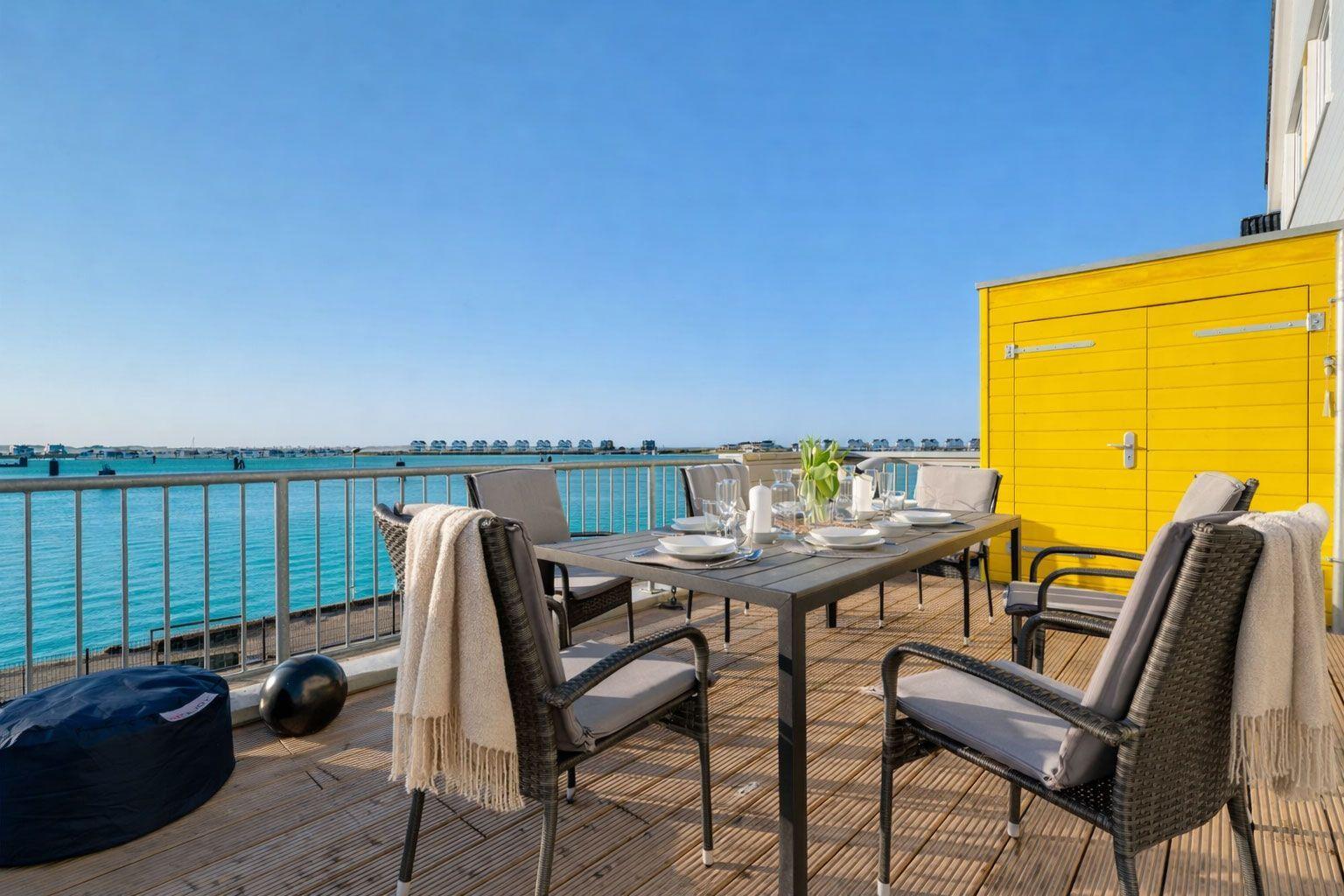 Terrasse mit Tisch, Stühlen und Meerblick. Gelber Schuppen und Sonnenschutz.