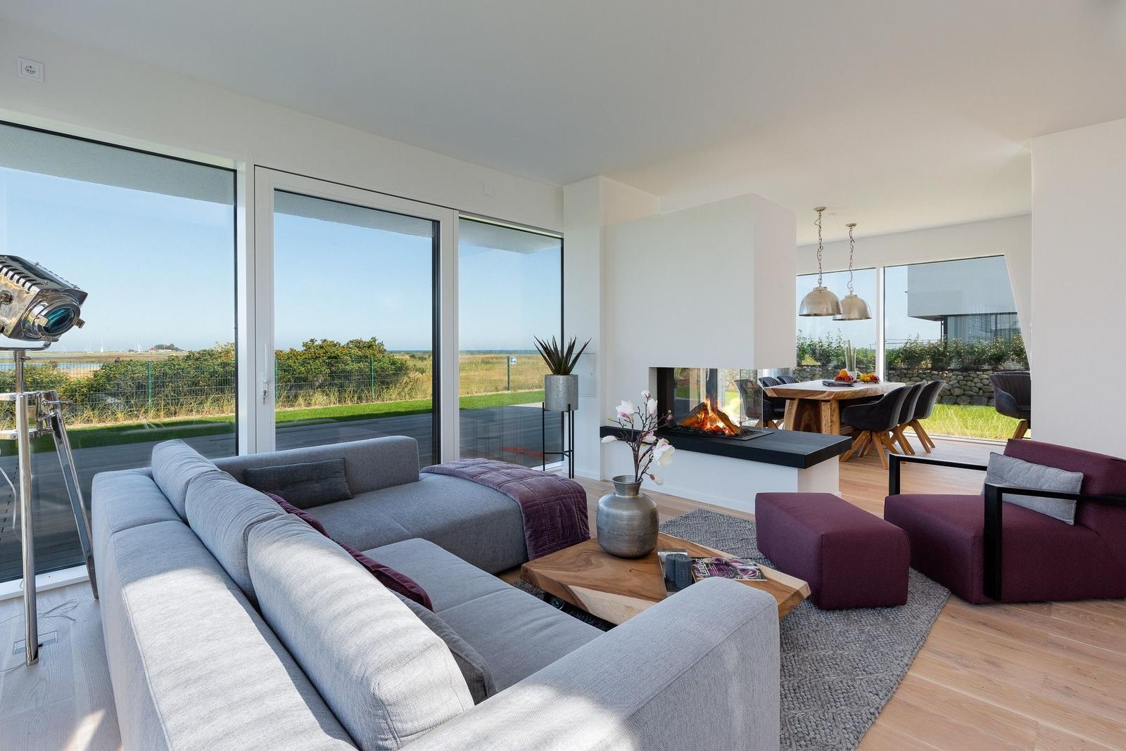 Wohnbereich mit Sofa, Kamin und Blick auf den Strand.