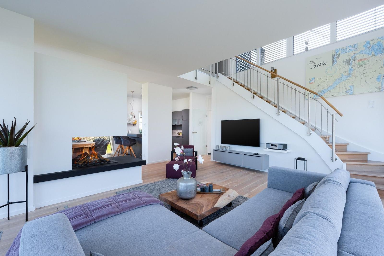Wohnzimmer mit Kamin, Sofa und Treppenhaus. Wandkarte und Fernseher sichtbar.