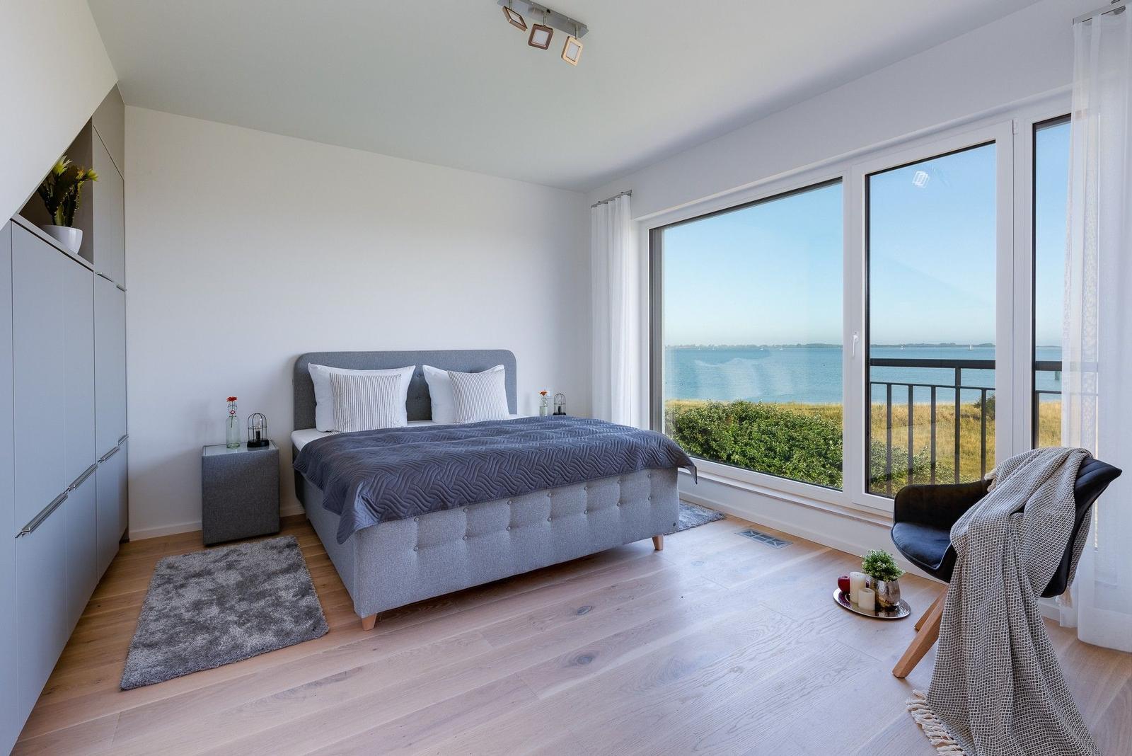 Schlafzimmer mit großem Fenster und Meerblick. Bett, Schrank und Sessel sind vorhanden.
