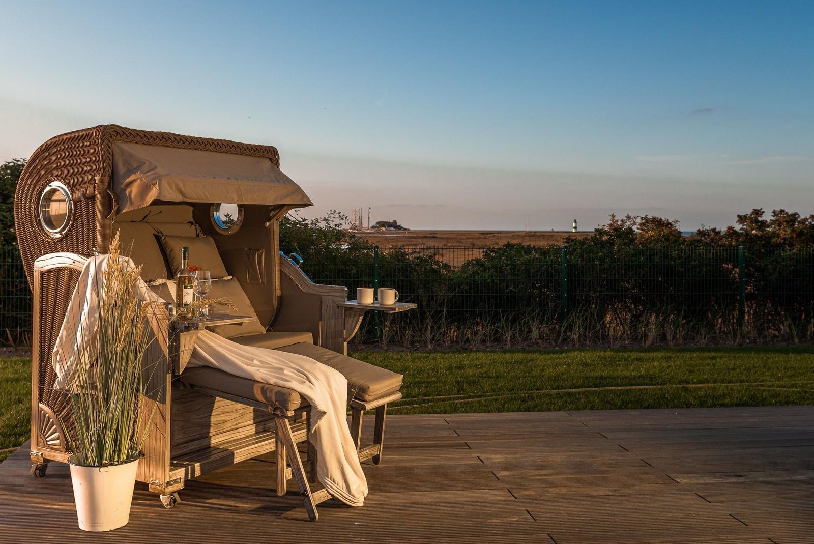 Rattan-Sonnenschutz mit Tisch und Getränken auf Holzterrasse. Blick auf Grünfläche und Horizont.