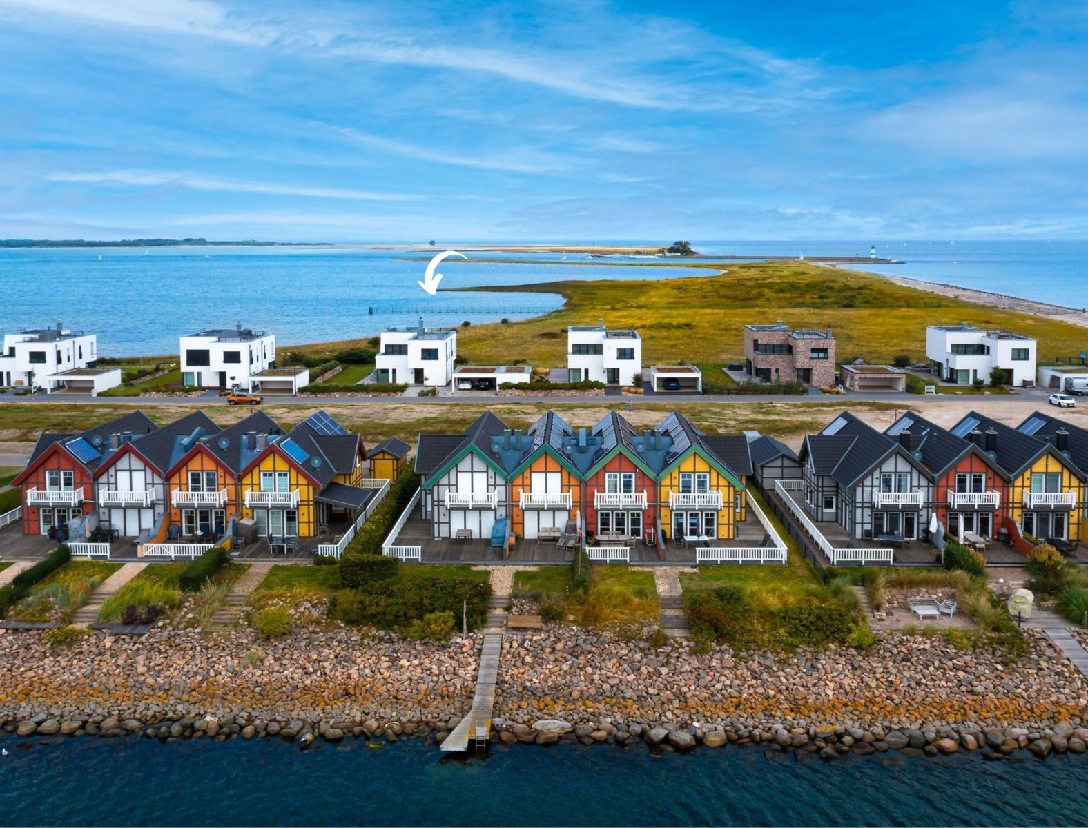 Farbenfrohe Häuser am Wasser mit Steinhäusern und modernen Villen im Hintergrund.