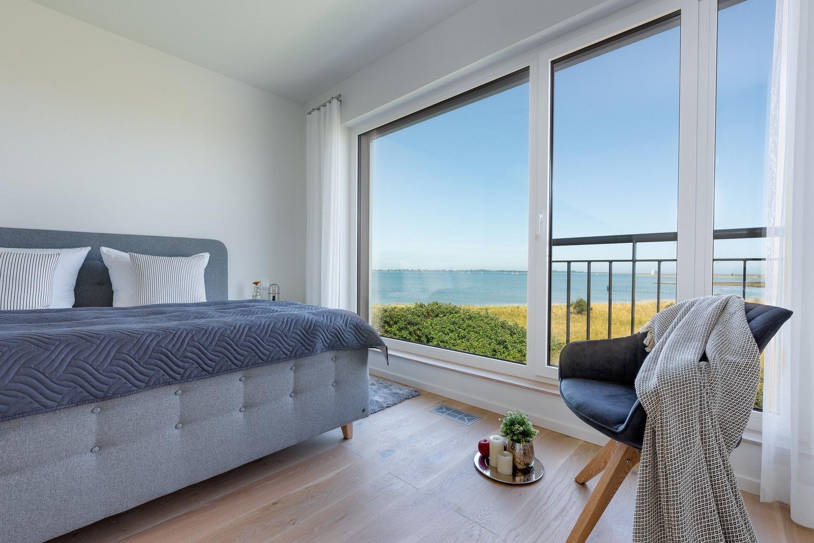 Schlafzimmer mit Blick aufs Meer und Balkon. Bett, Stuhl und Holzboden.