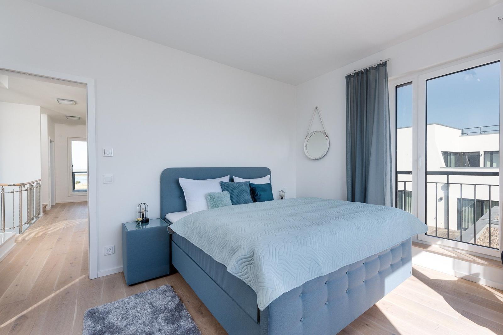 Schlafzimmer mit blauer Bettwäsche und großem Fenster zum Balkon.