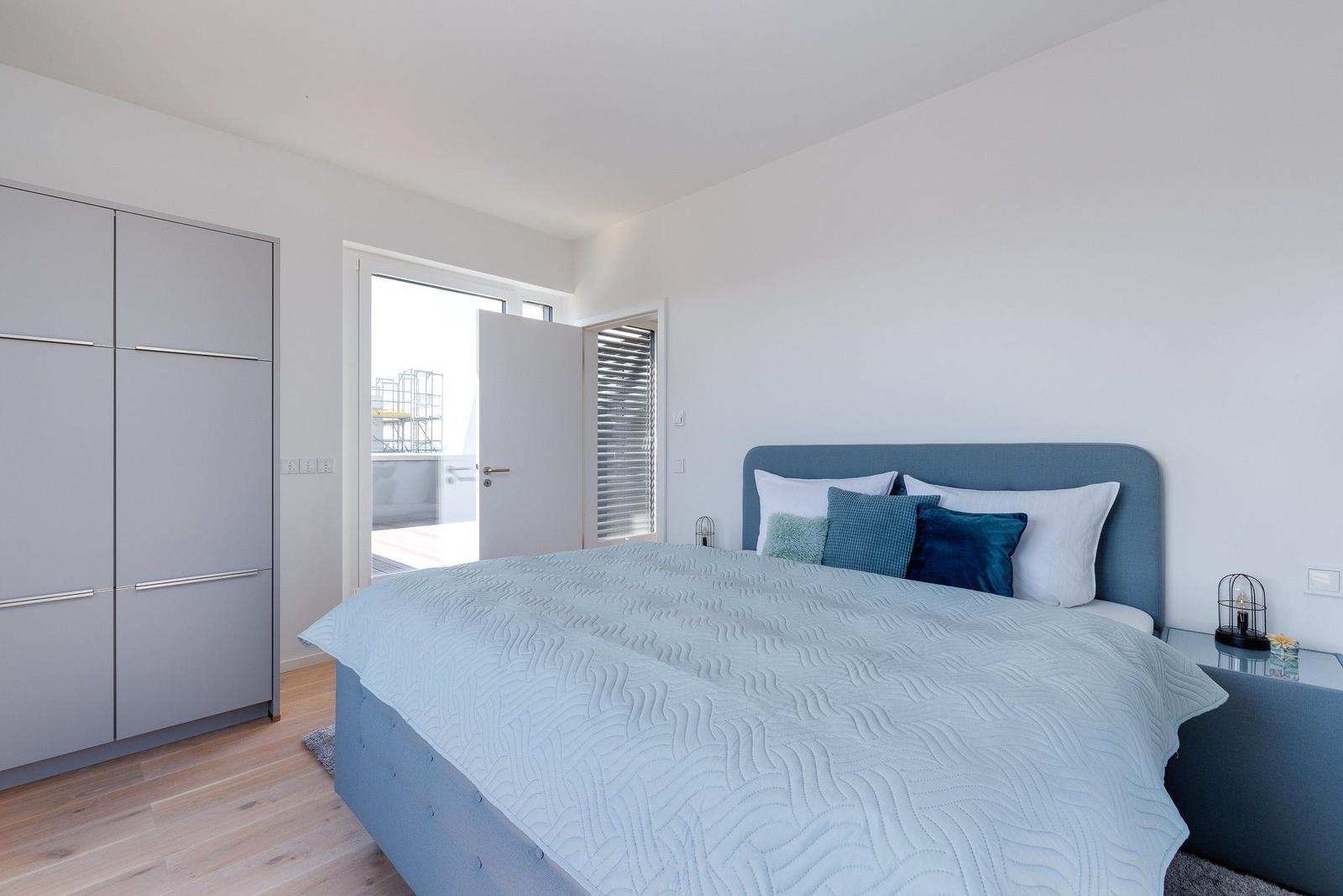 Schlafzimmer mit Bett, Kleiderschrank und Tür zum Balkon.