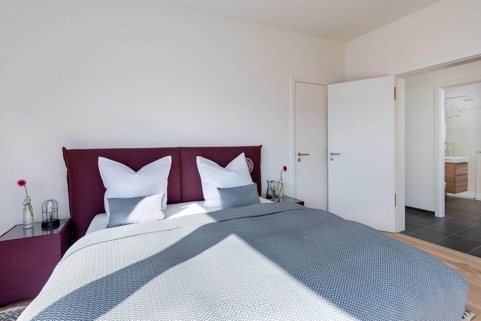Schlafzimmer mit Bett, Kopfteil und Nachttisch. Blick in das Badezimmer.