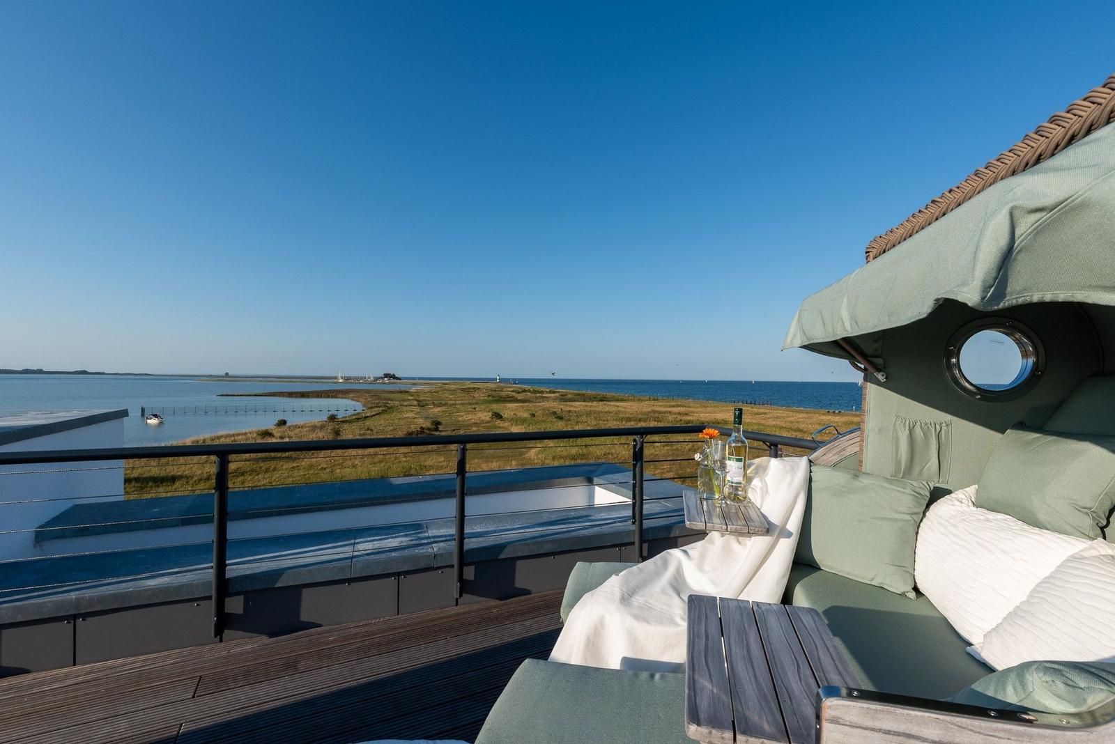 Terrasse mit Sitzgelegenheit und Blick auf Wasser und Grasland.
