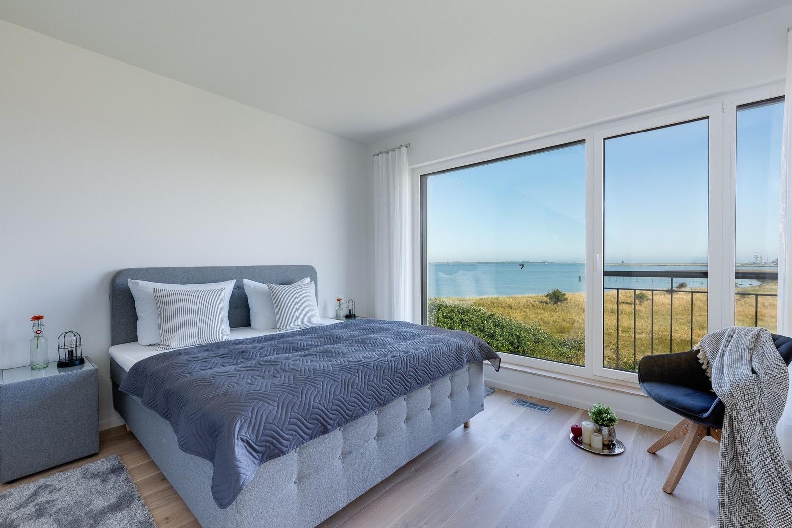 Schlafzimmer mit Blick aufs Meer und Balkon. Bett, Nachttisch und Stuhl.