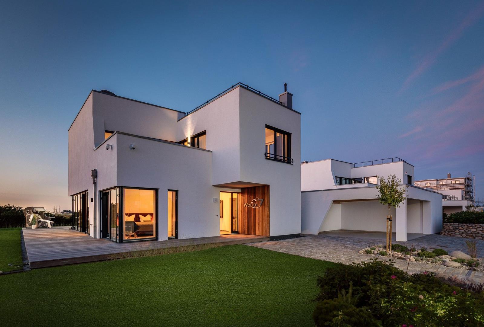 Moderne Villa mit großem Garten und Holzterrasse bei Dämmerung.