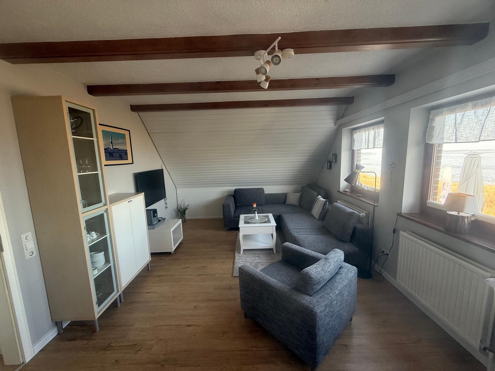 Wohnzimmer mit Sofa, Sessel und TV. Holzbalken und Fenster mit Blick.