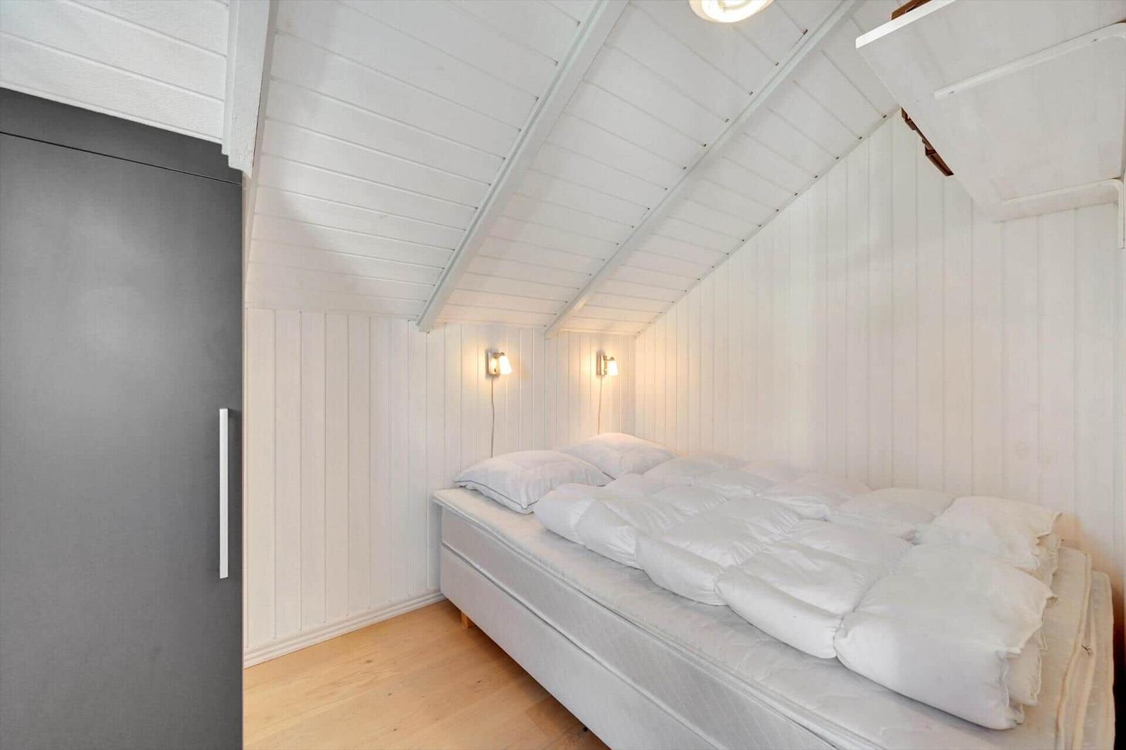 Bedroom with white bed, wooden floor, and white walls under sloped ceiling.