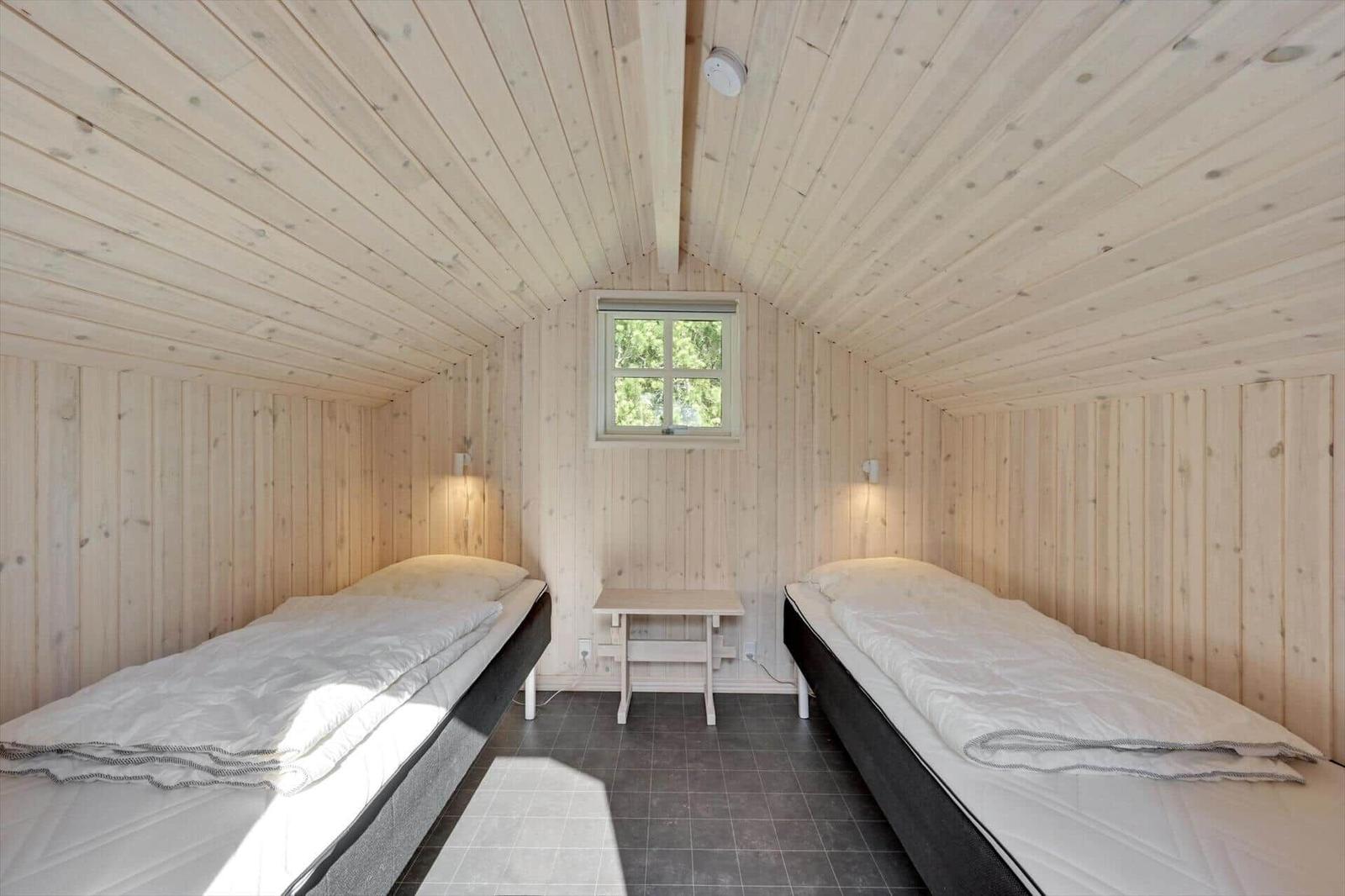 Two beds in a wooden room with window and table.