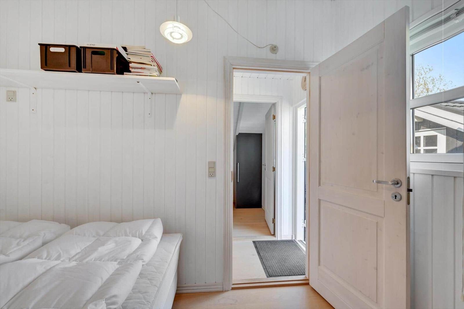 Bedroom with white bed, wooden wall, and door to hallway.