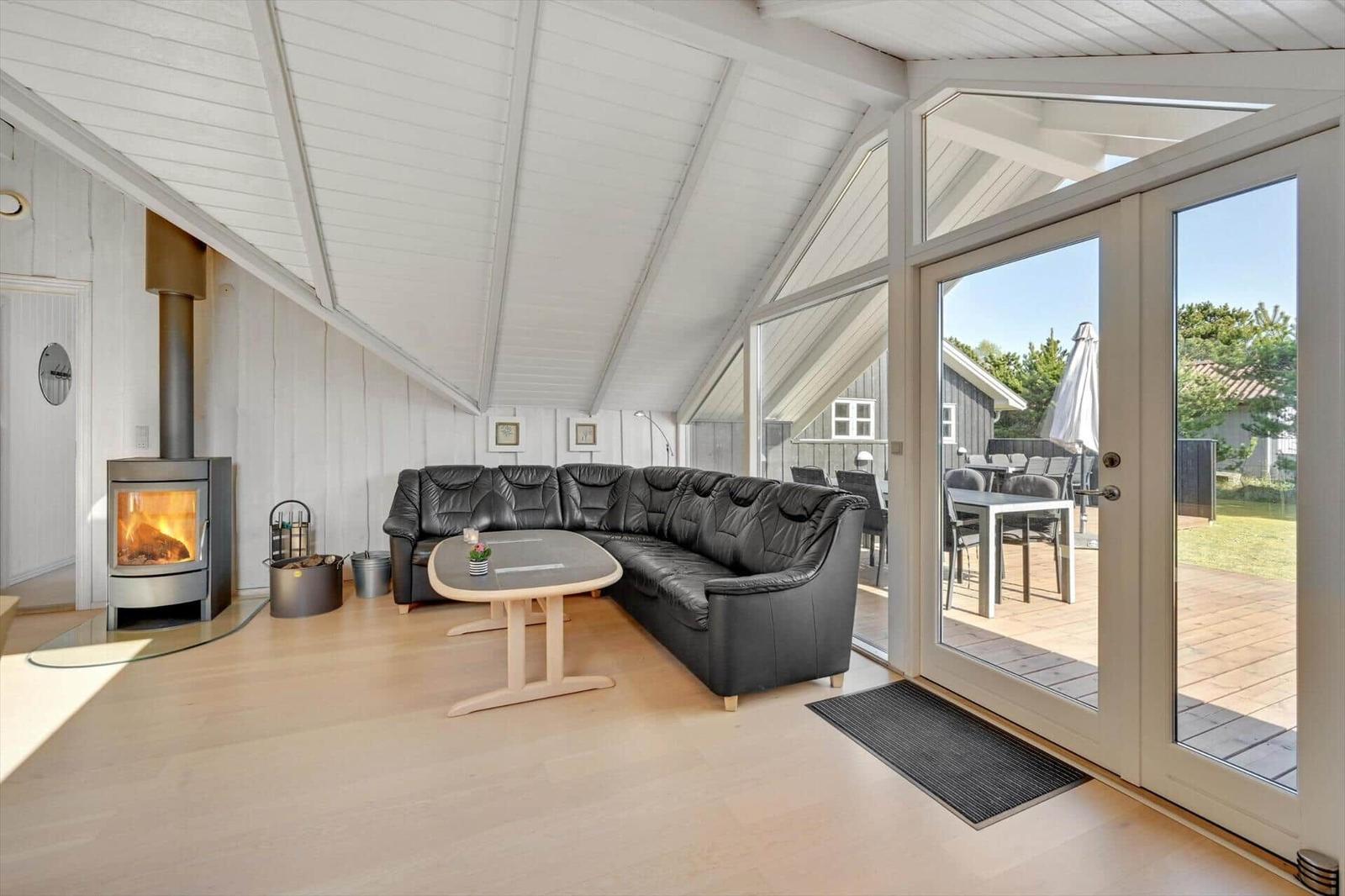 Living area with black sofa, wooden table, and fireplace. Entrance to terrace with table and chairs.