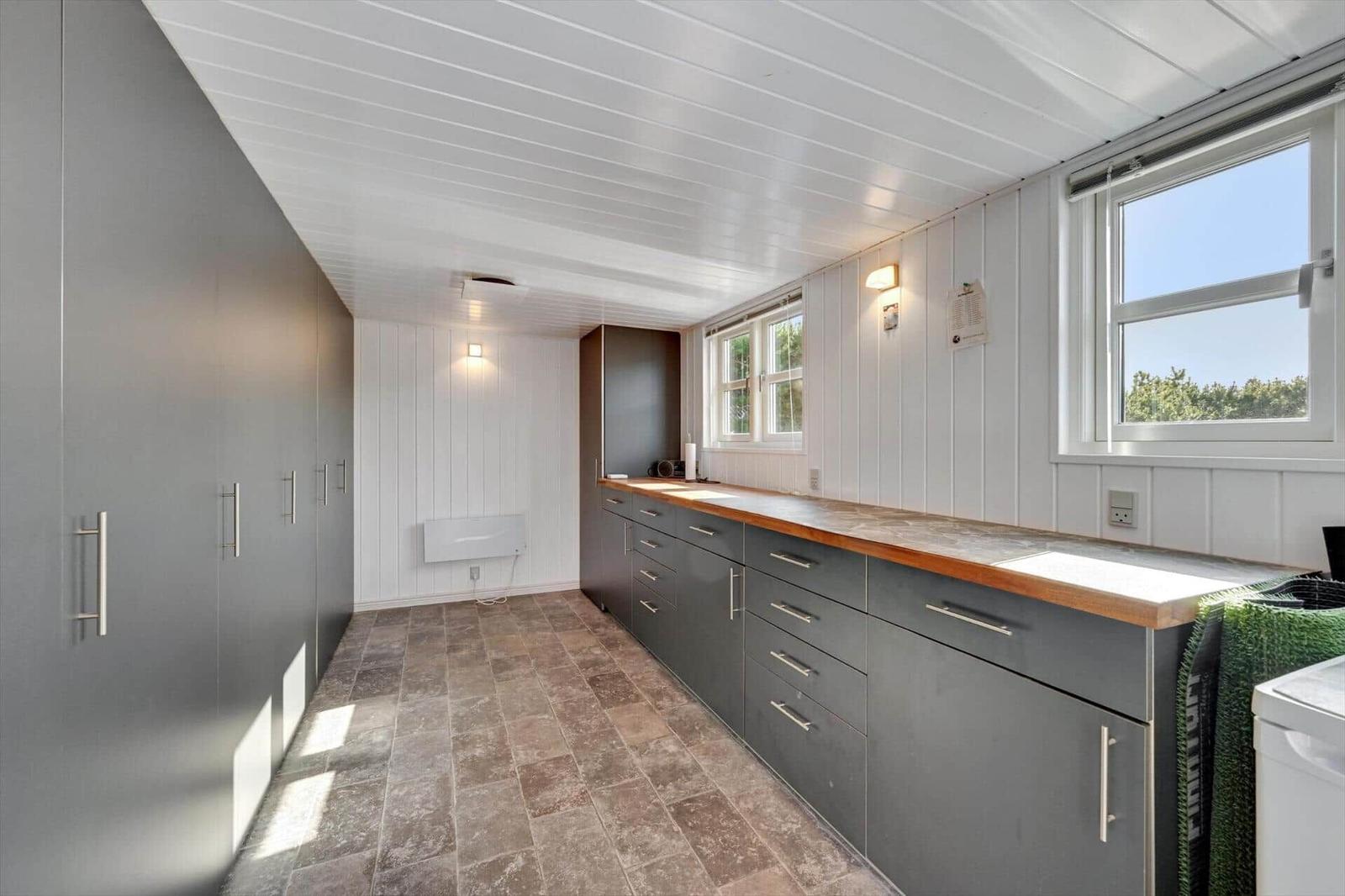 Kitchen with gray cabinets, wooden countertop, and windows. Tile floor and white walls.