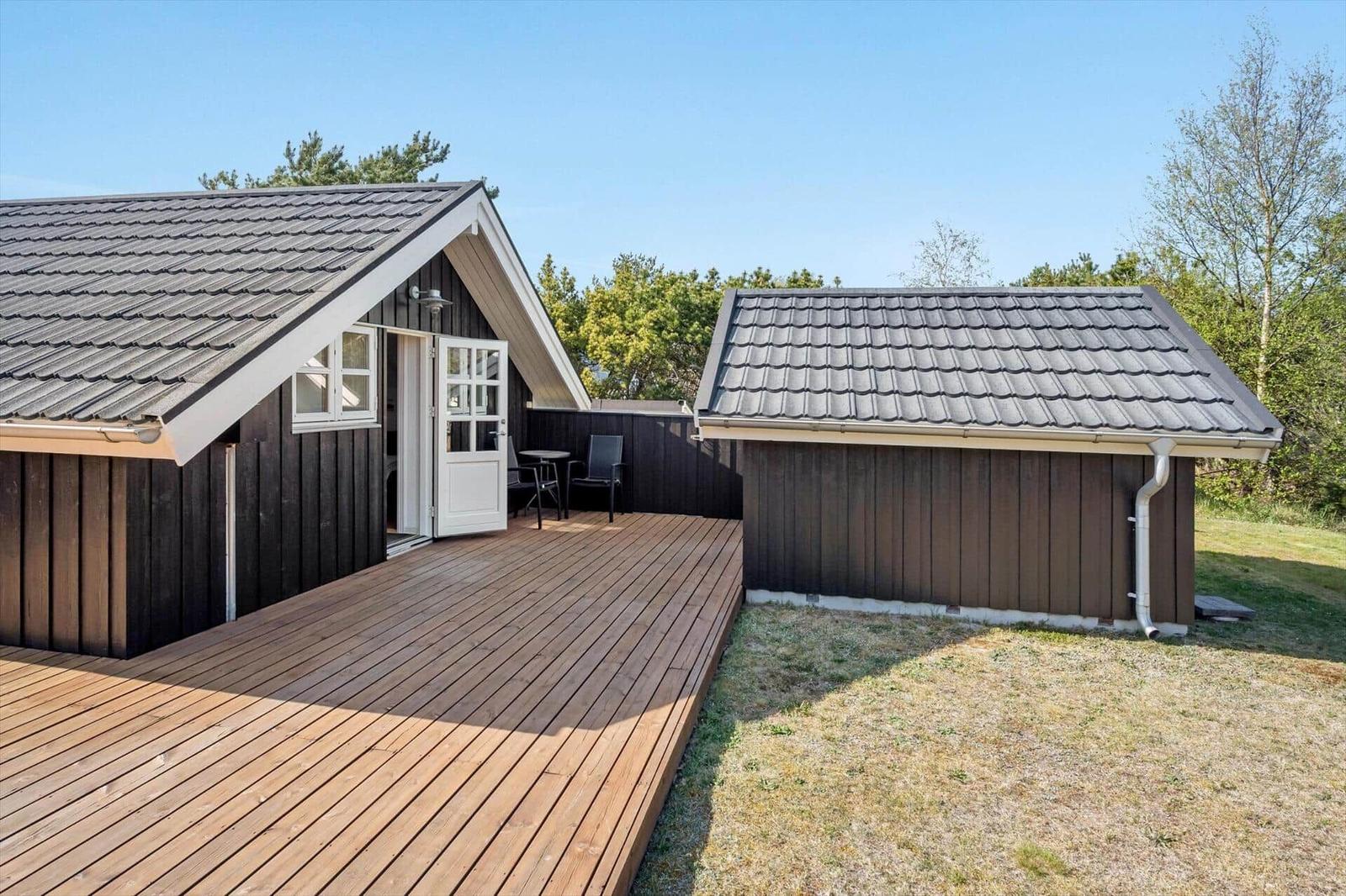 Wooden cabin with terrace and garden. White door and windows. Roof with shingles.