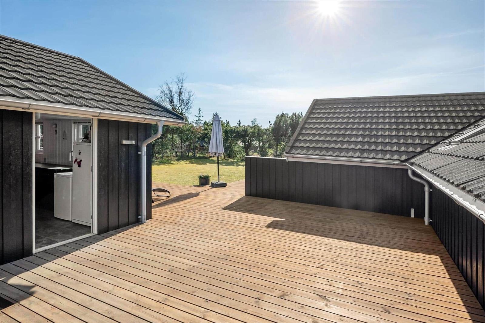 Wooden terrace with view of lawn and houses. Sunny day with shadows cast.