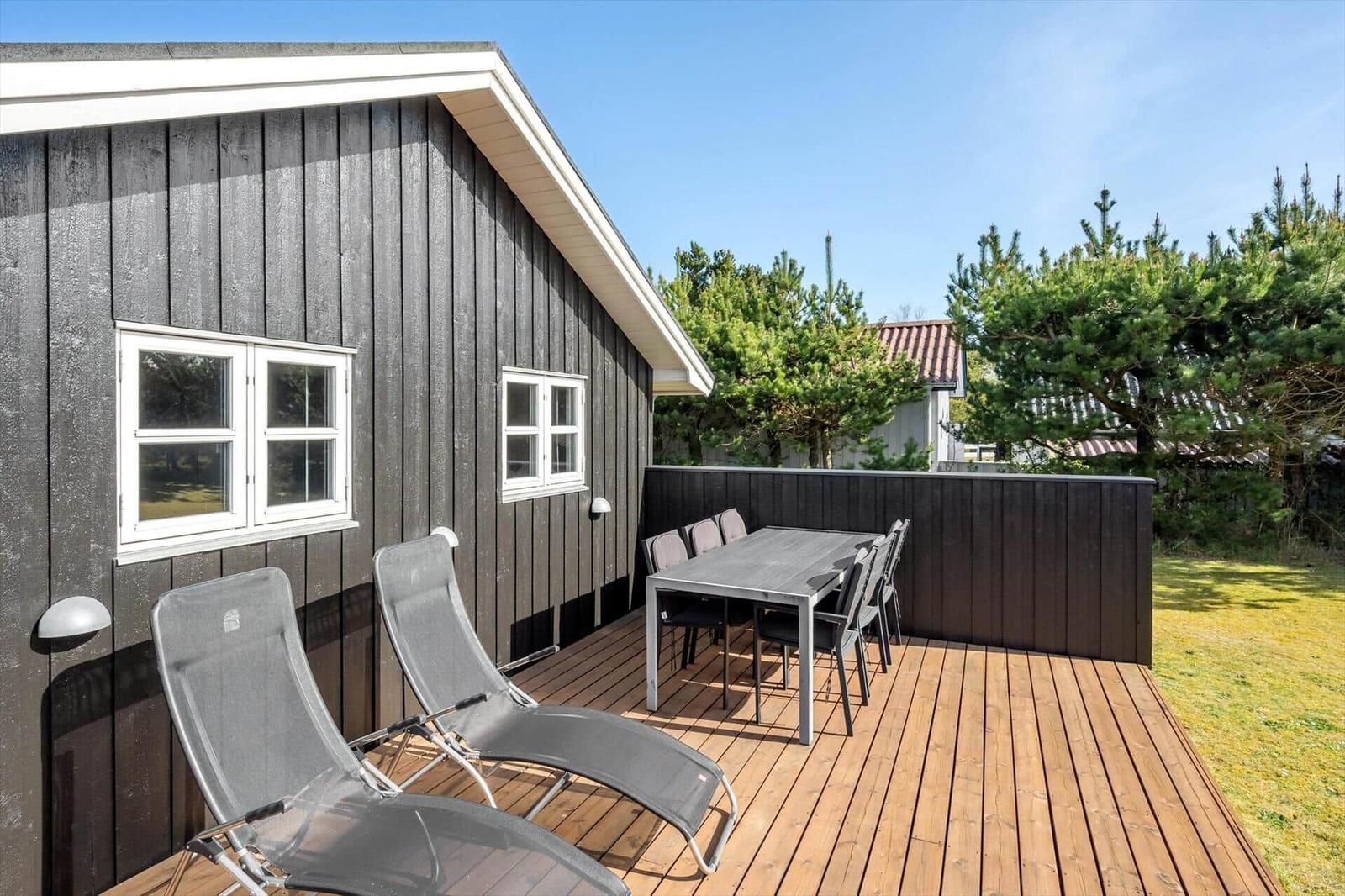 Deck with table, chairs, and loungers beside a house with dark siding.