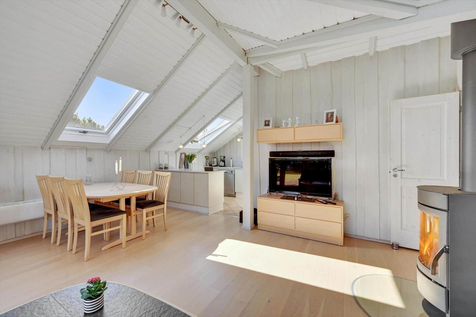 Living and dining area with wooden floor, skylights, and wood stove.