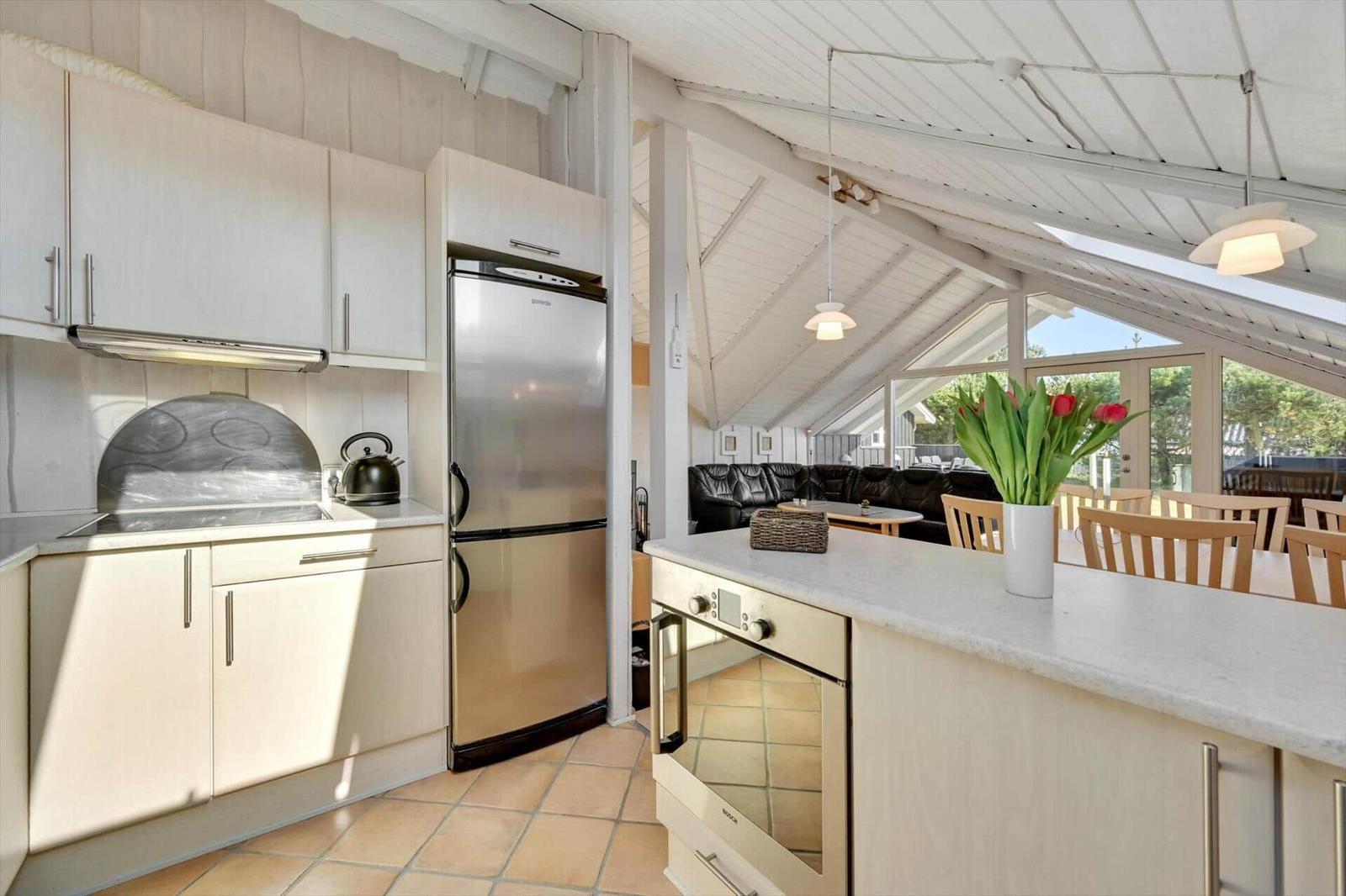 Kitchen with refrigerator, stove, and countertop. Living area with sofa and table in background.