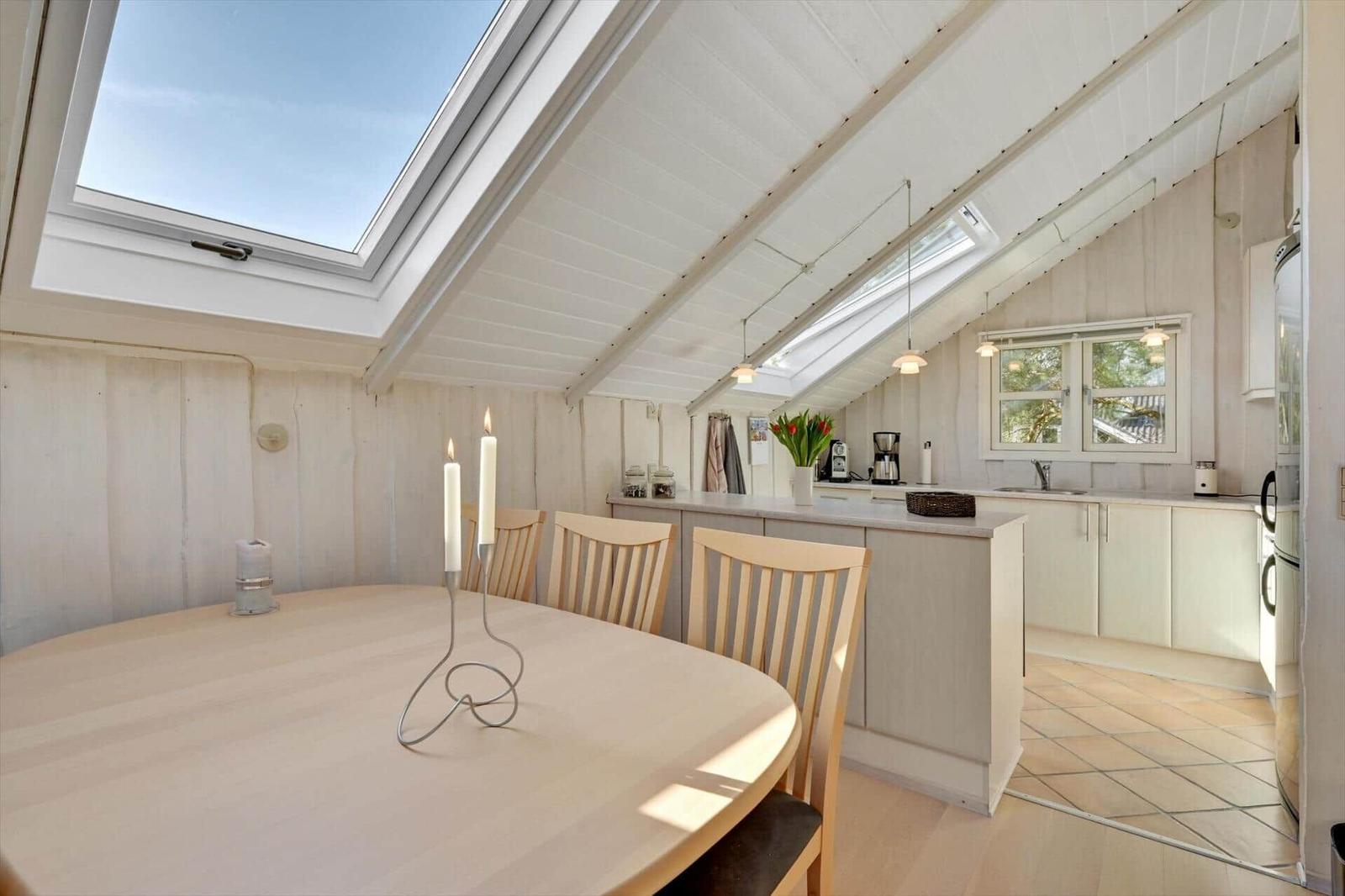 Dining area with round table and chairs under sloped roof with skylight.