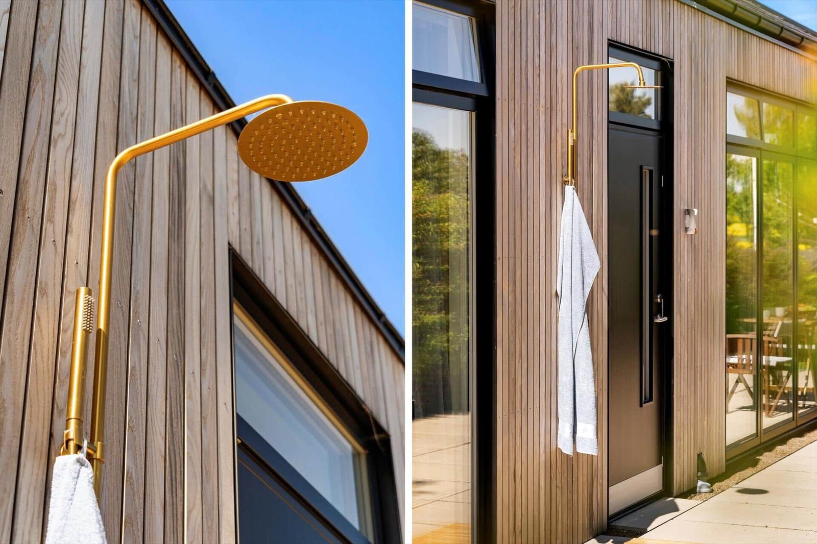 Outdoor shower with gold head mounted on wooden wall beside entrance door
